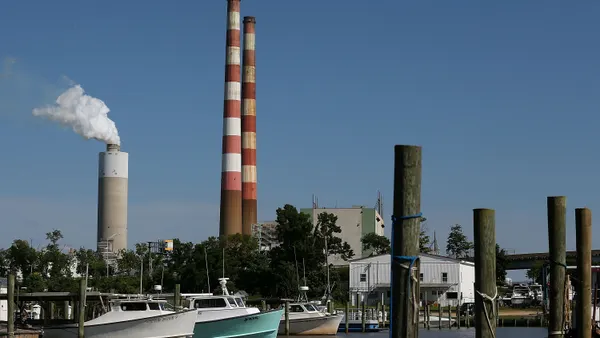 Boats are moored on a river with a power plant's smokestacks in the background.