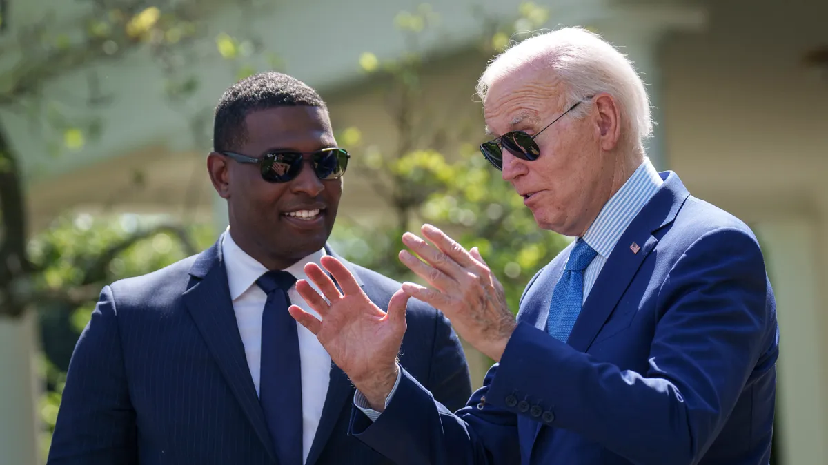 Two people wearing sunglasses talk to each other in front of a blurred background