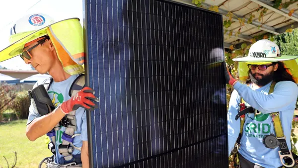 Picture shows solar installers carrying a panel.