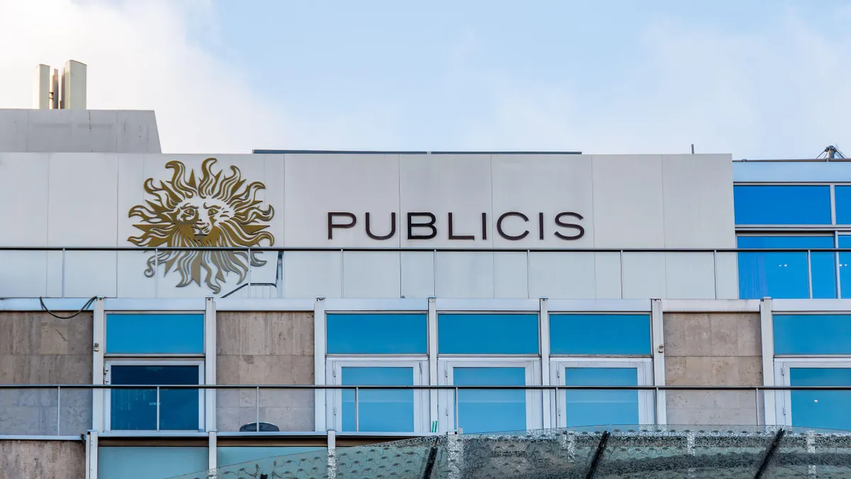 Building facade with large windows and a white panel displaying a golden lion logo next to the word “PUBLICIS” in thin capital letters.