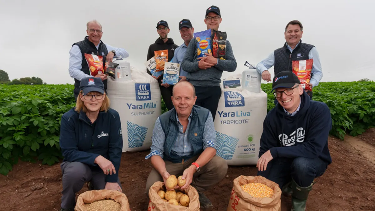 A group of people stand in a farm field with potatoes and bags of fertilizer