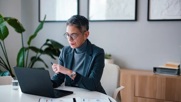 A business person reviews documents while working on a laptop in a professional office.