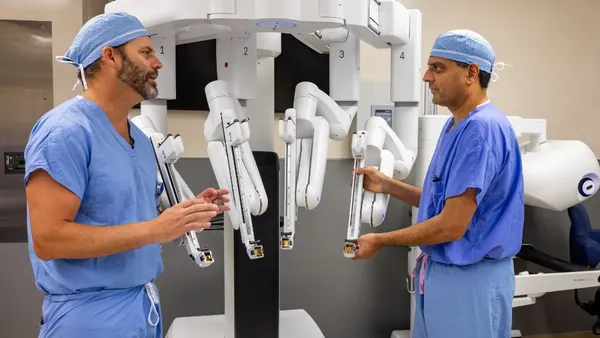 Two clinicians wearing scrubs stand in front of Intuitive Surgical's da Vinci 5 robotic surgery system.