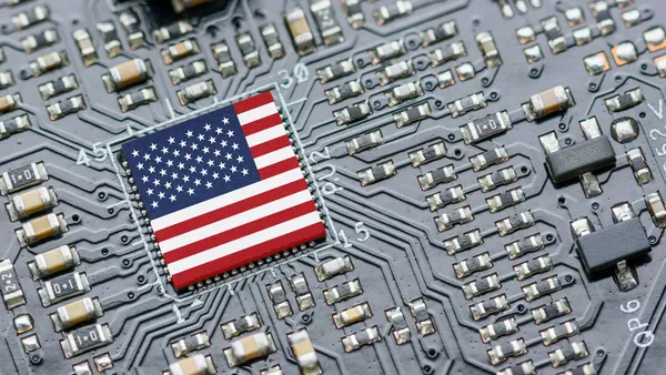 The United States flag as a microchip in the center of a gray motherboard.