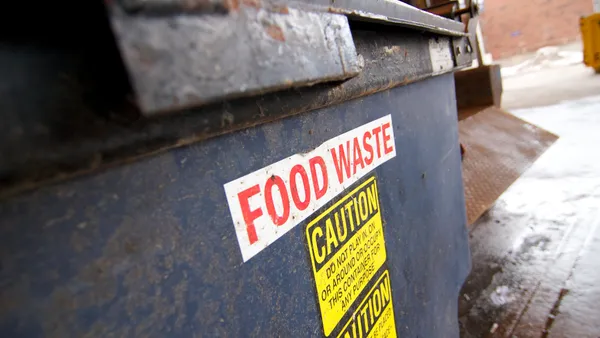 Close-up photograph of a dumpster with a sign that says "food waste"