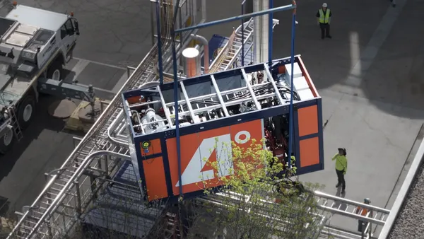 A piece of industrial equipment is lowered into place, with workers on the side