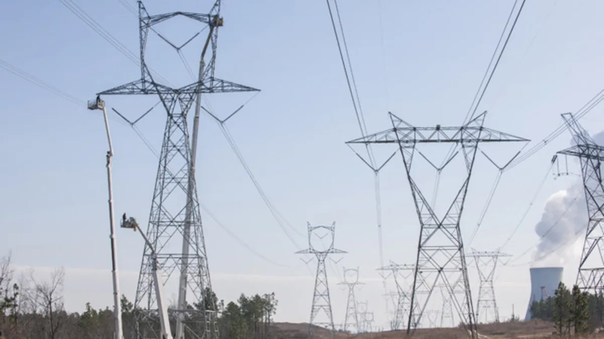 Three sets of transmission lines run into the distance where steam billows from a cylindrical, cement structure.