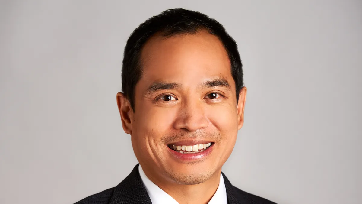 A headshot of Chemours Co.'s new CFO, Jonathan Lock smiling wearing a black suit jacket, white shirt, purple tie, with a grayish-tan background.