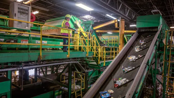 A worker in a hard hat looks at a conveyor belt with recyclable materials