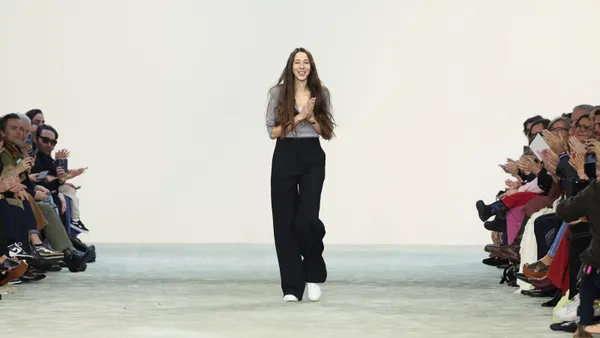 A person with very long, straight hair stands at the end of an empty runway with clasped hands.