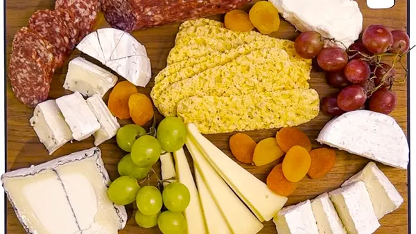 Cutting board displaying a variety of cheeses, crackers and grapes