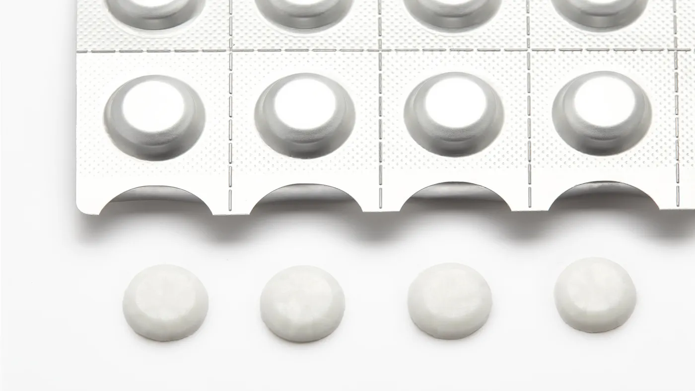 A blister pack with six pills inside rests above three white tablets on a white background. The layout is orderly, conveying a clinical tone.