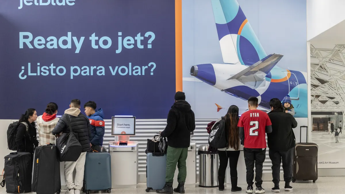 Travelers with their bags stand in front of a JetBlue sign that reads "Ready to jet?"