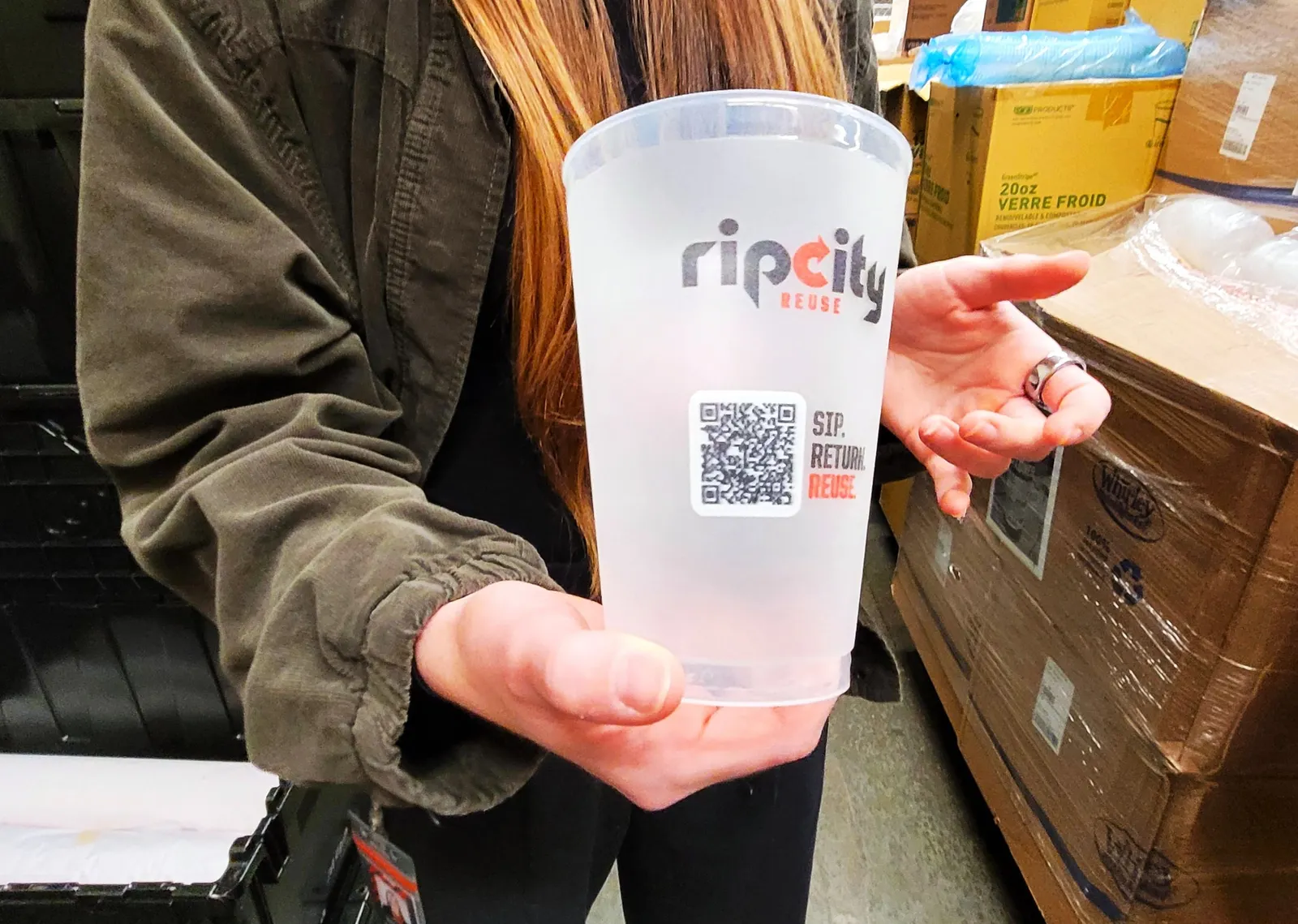 A person holds a plastic cup that says Rip City Reuse and which features a QR code.