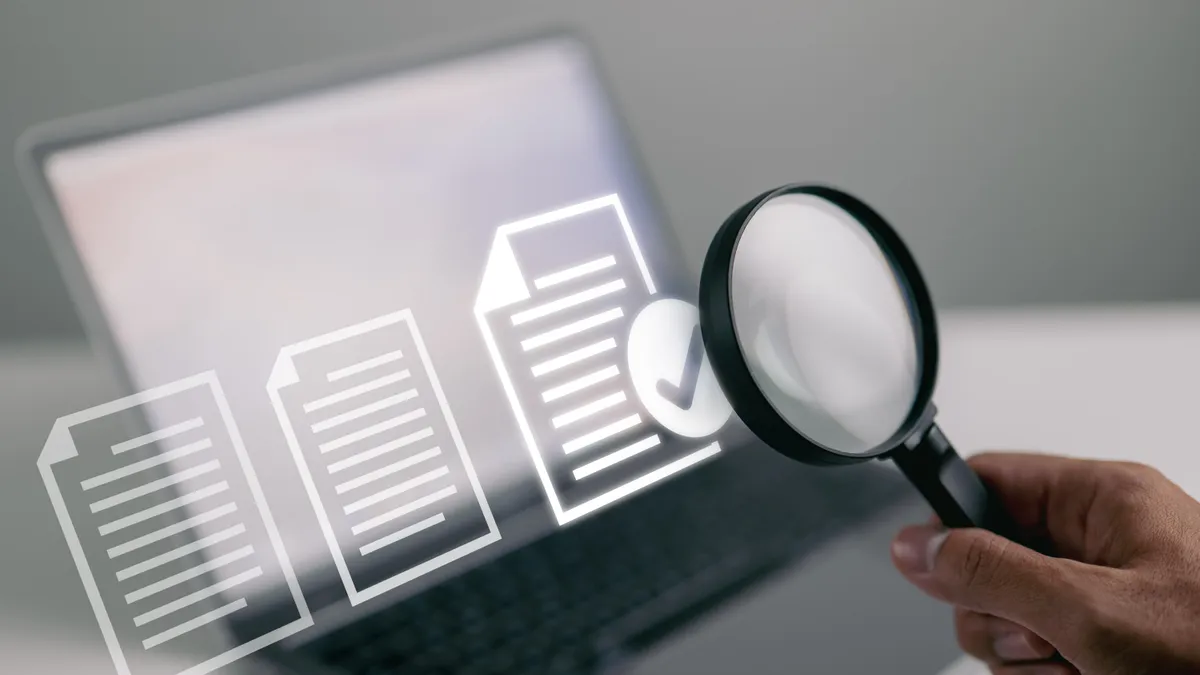 A magnifying glass pointing at documents on a laptop