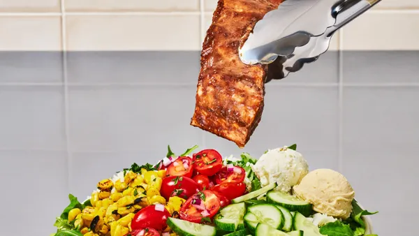 A photograph of salmon held in tongs over a bowl of various vegetables, rice and greens.