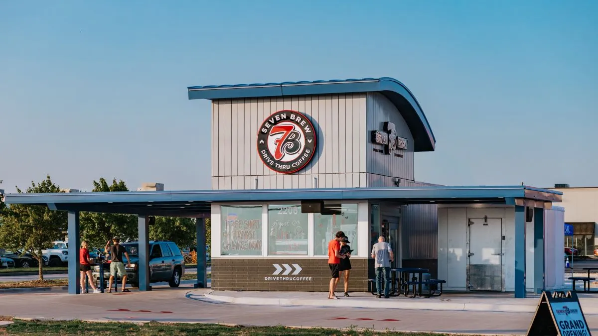 An image of a small restaurant with people gathered around. Thereis 7 Brew signage.