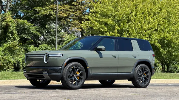 A Rivian R2 crossover SUV sits on gravel, with green trees in the background.