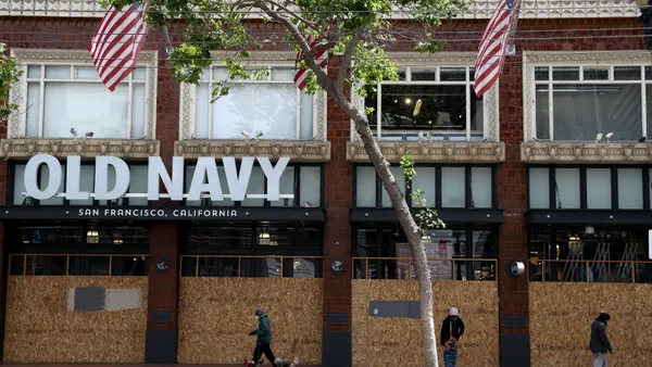 Shoppers walk by boarded-up windows in front of a brick, Old Navy building.