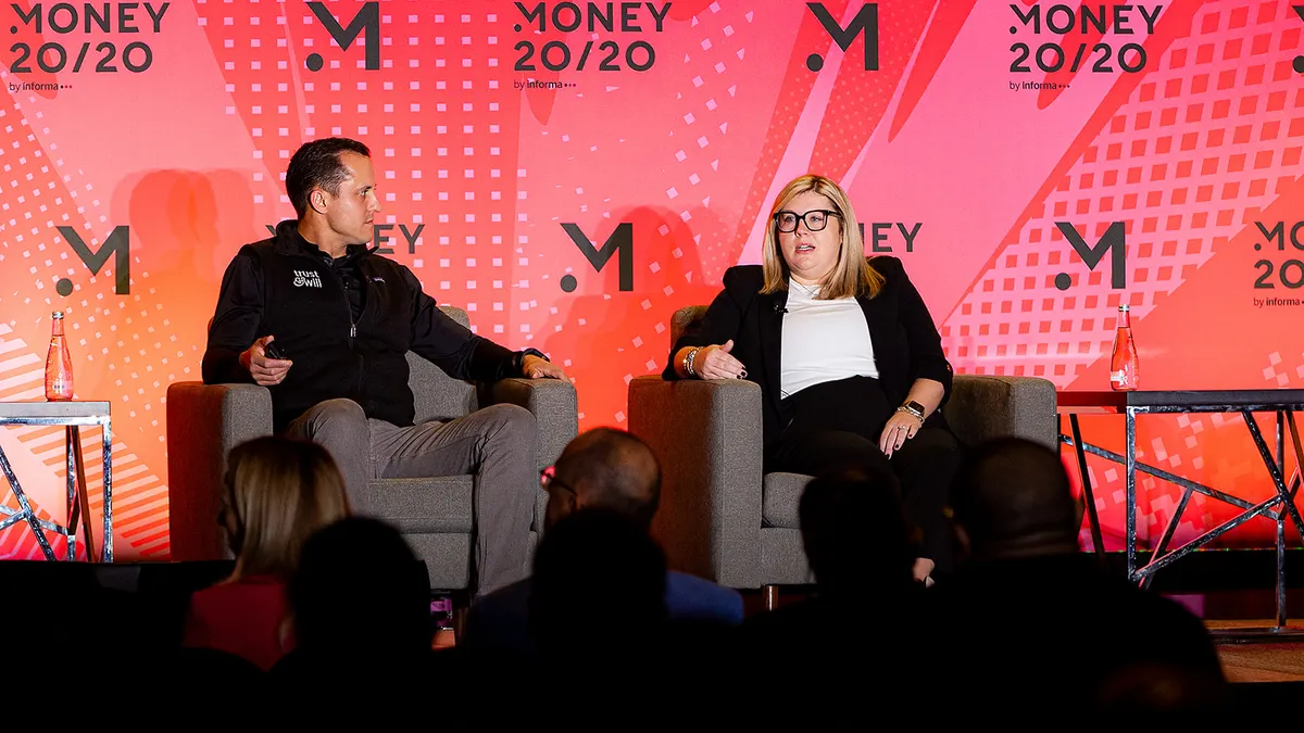 Erin Crawford speaks while sitting on the right side of a stage, in conversation with another person.