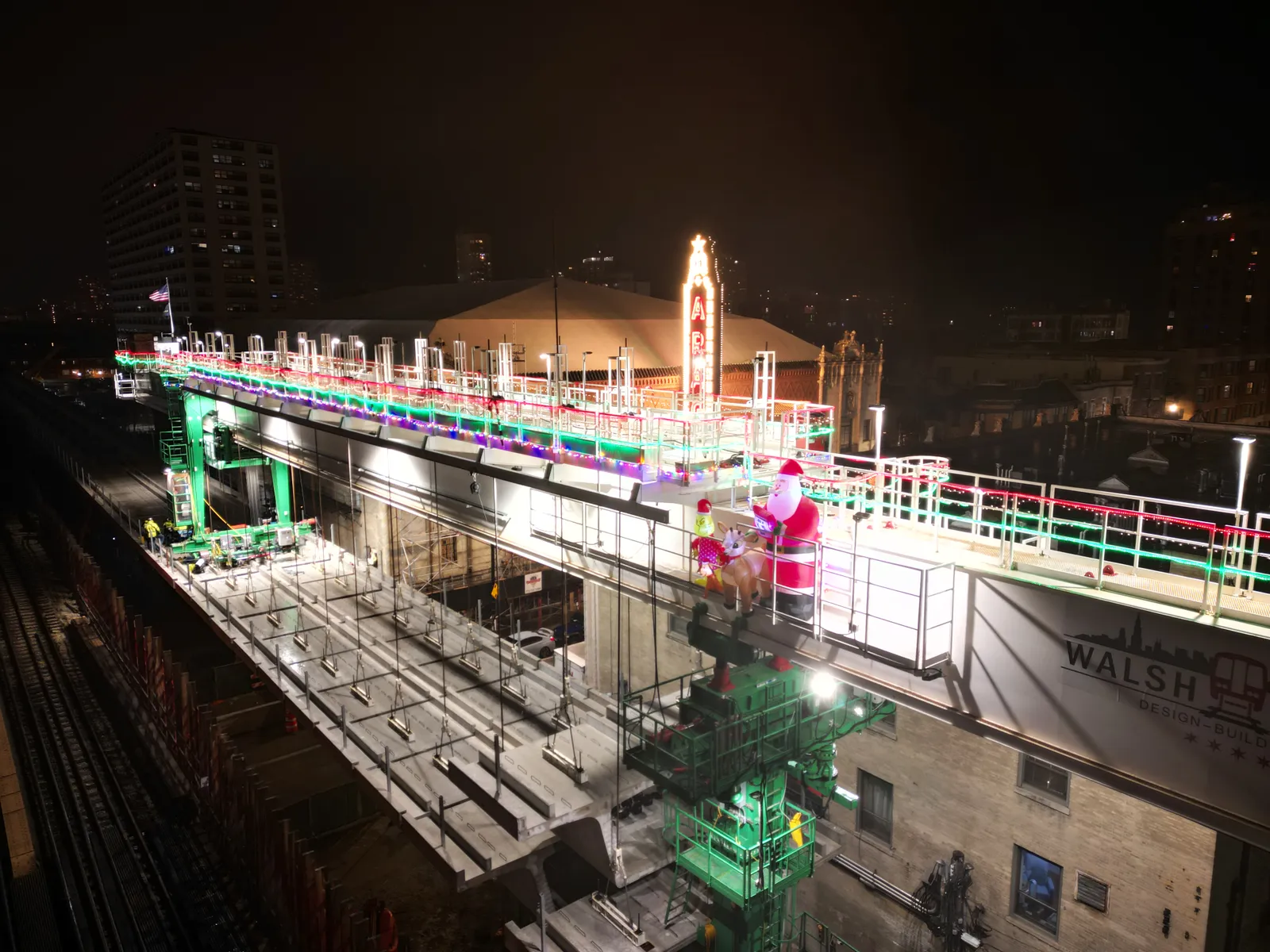 A large gantry used to install precast concrete is lit up with many holiday lights. It's lit up against the night sky in Chicago.