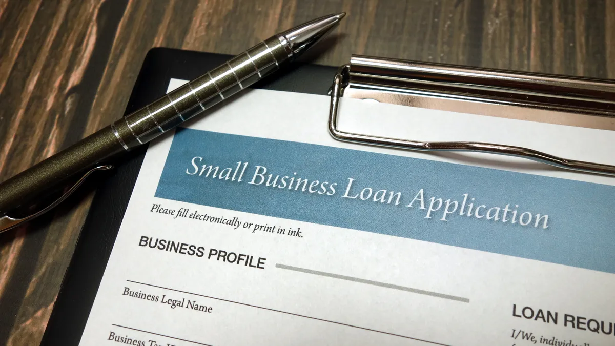 Clipboard with small business loan application form and pen on wooden desk background.