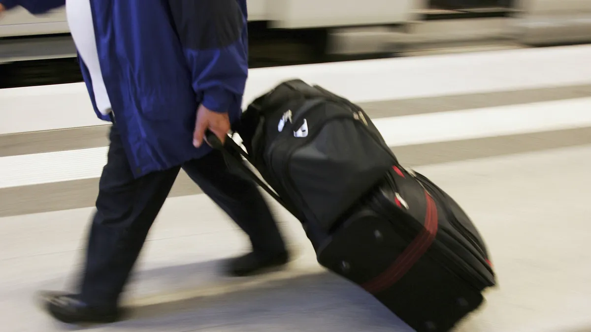 A blurry photo of a person pulling a suitcase behind them from the waist down.