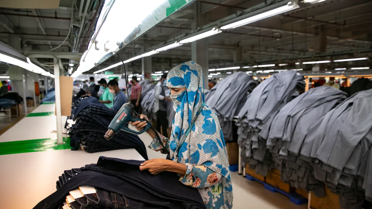 Workers in a line complete work on piles of pants.