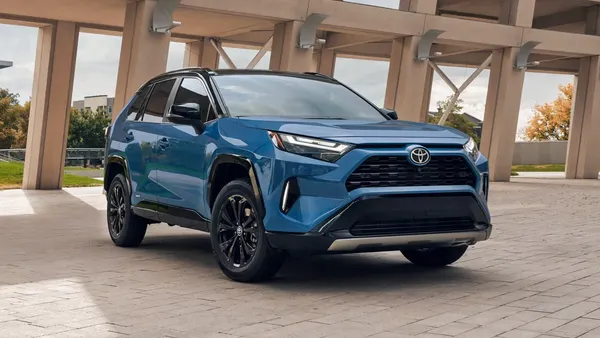 A blue 2025 Toyota RAV4 SUV parked outdoors with a concrete structure in the background.