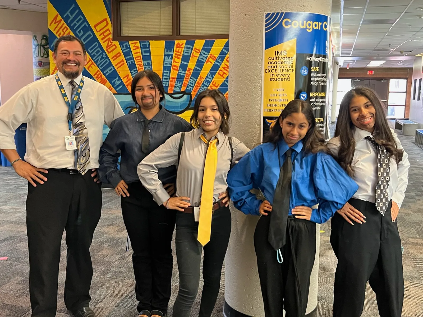 A man middle school principal stands in a school hallway with four girl students who have dressed like him for Dress Like a Teacher Day.