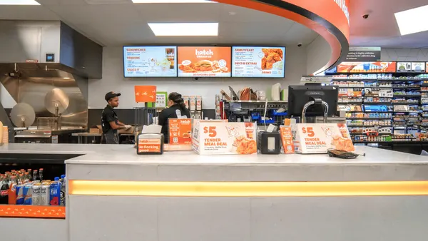 A photo of the interior of a convenience store, looking at a foodservice counter. A sign over the counter says "Brighten up your meals with Hatch."