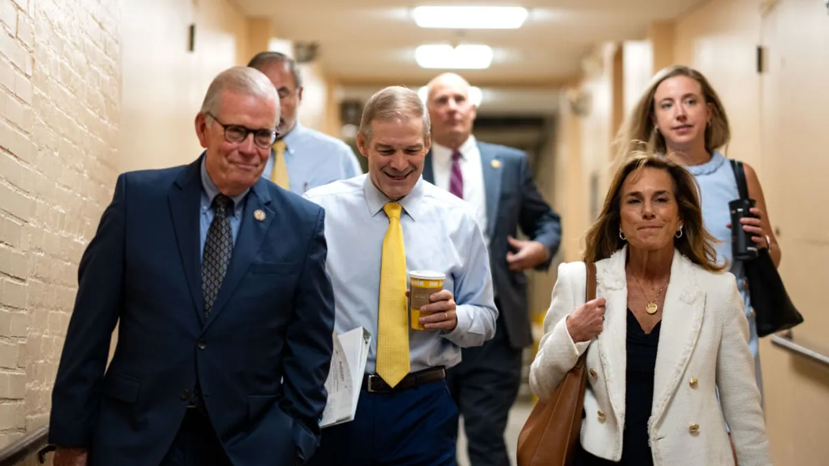 A handful of people are walking toward the camera. They are walking in a hallway