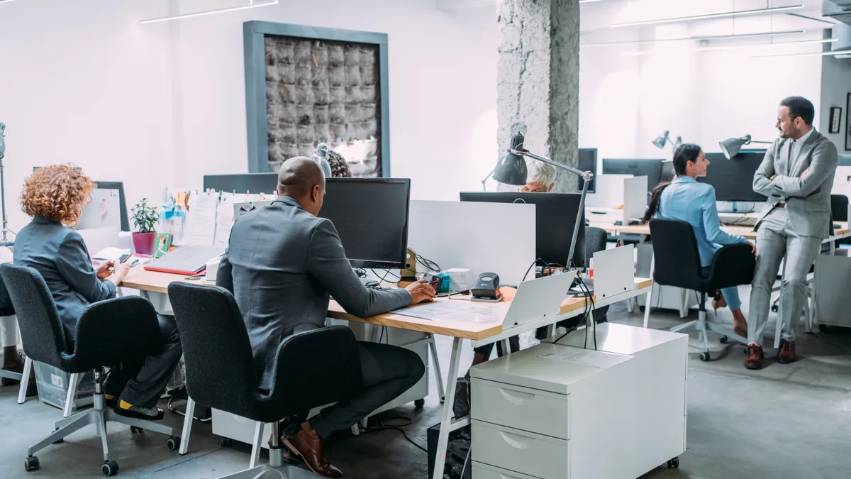 Employees work in an office, with two conversing in the background.