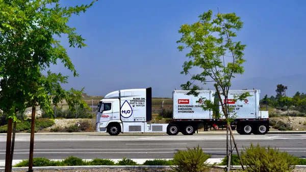 A Hyundai Xcient hydrogen fuel cell truck shown from the side with trees in the foreground and branding stating that the truck runs on hydrogen and only emits water.