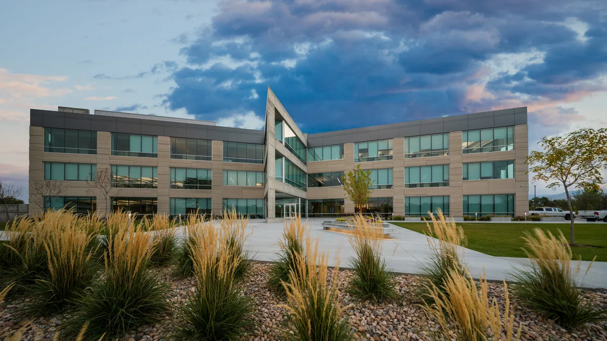 An angular building stands in focus with the sky in the background. There's stones and shrubs in the garden area in front of the building.