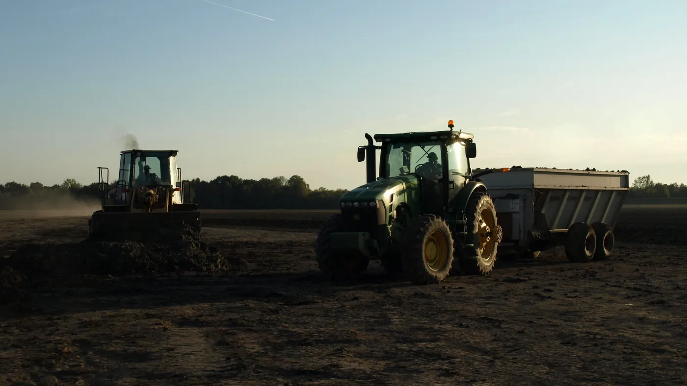 Two tractors move on a field against a clear sky.