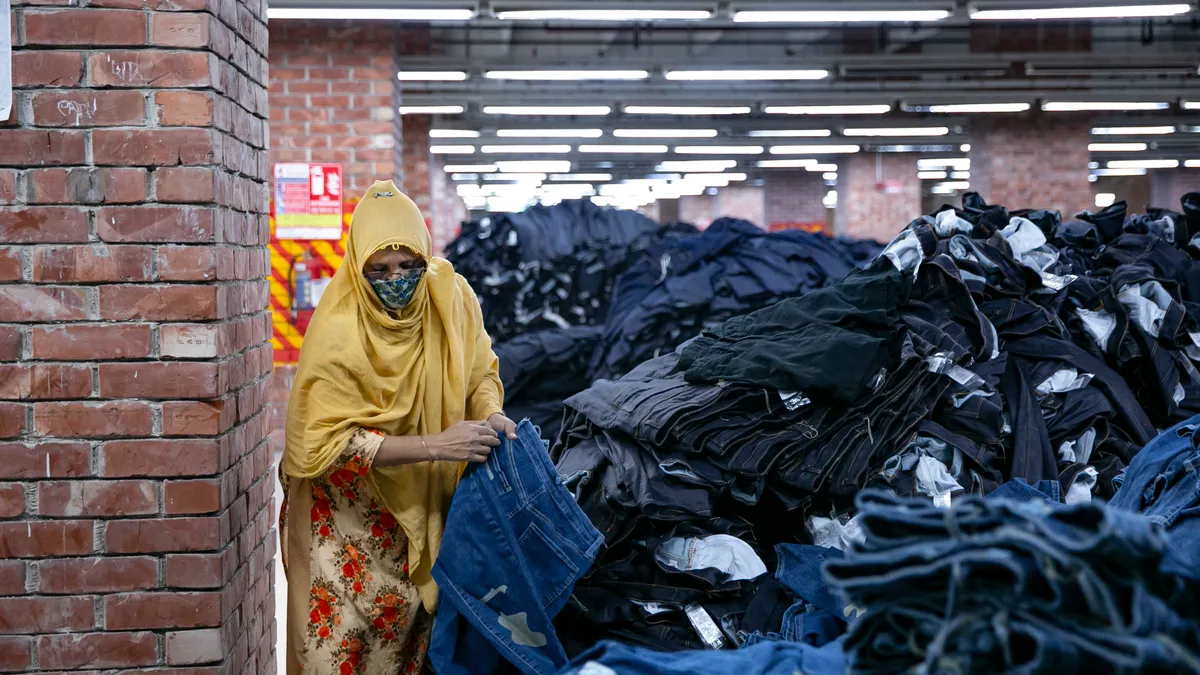 A garment worker in Bangladesh is seen holding a pair of jeans next to a pile of jeans.