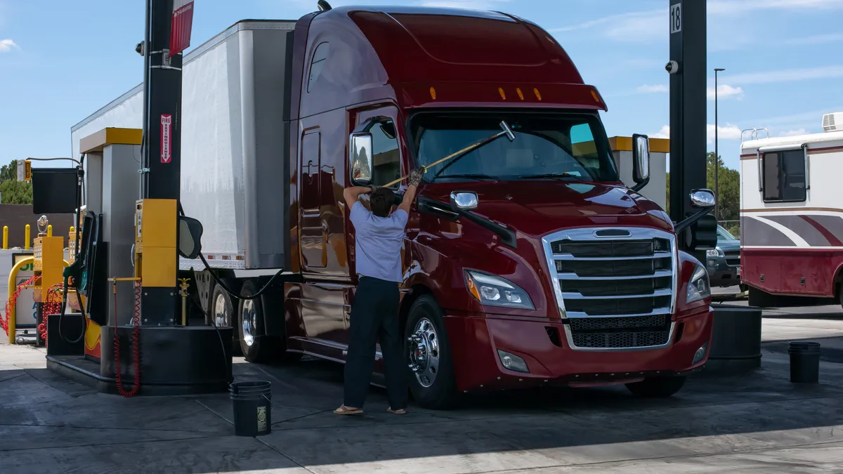 A man cleans the windshield of a tractor-trailer at a fueling station.