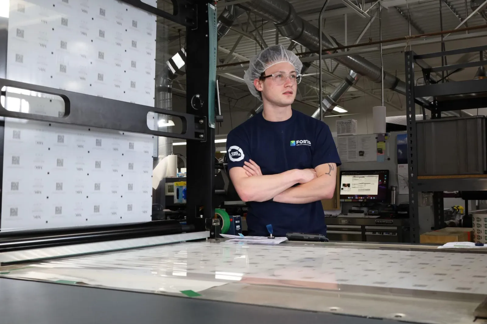 An employee with a hat and apron stands next to industrial printing equipment.