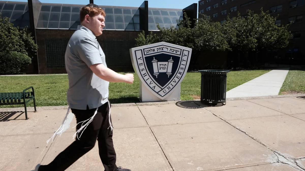 A person walks by a shield with Yeshiva University seal.