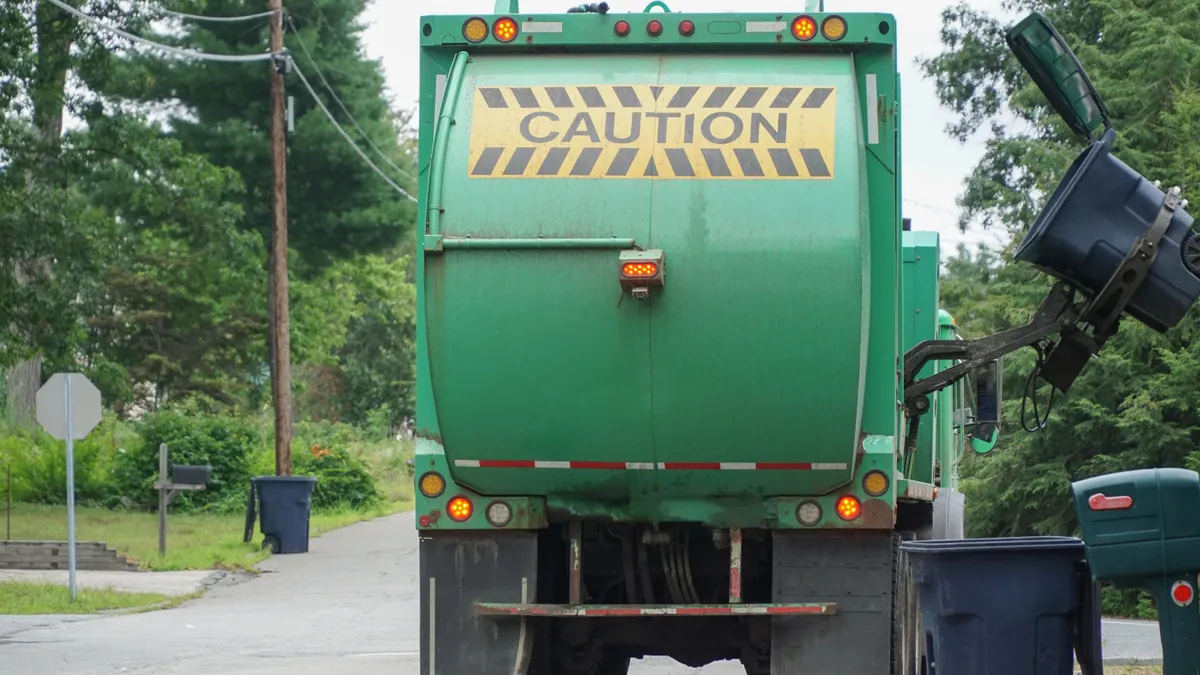 Rear view of a waste truck, with the word caution on its body, collecting a cart in a residential area