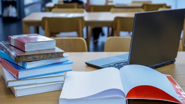 a desk in a classroom has a laptop and papers on it.