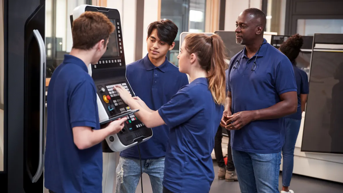 Four people in dark purple polo shirts working on a CNC machine.