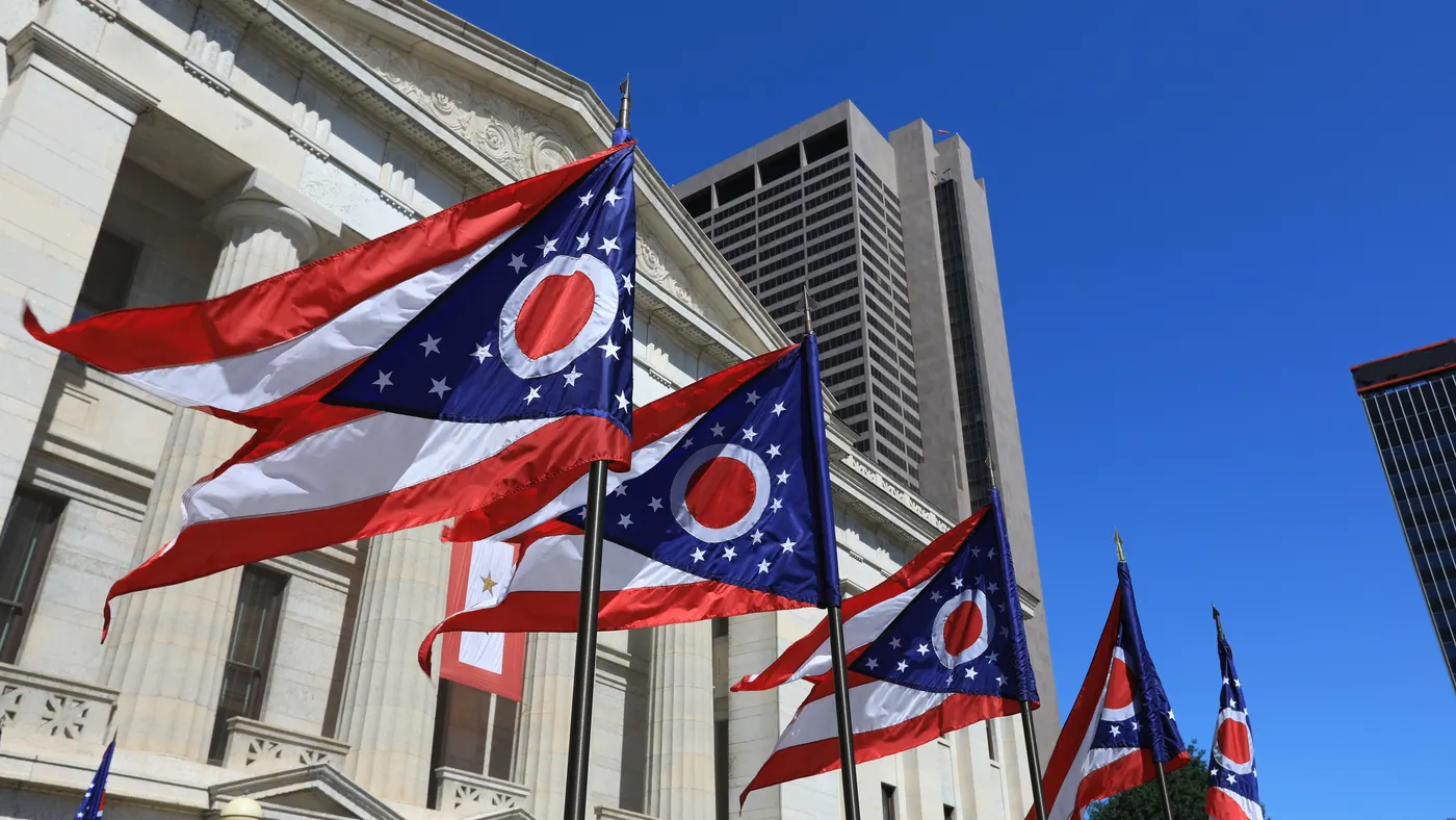 Several Ohio state flags fly outside of the statehouse building.