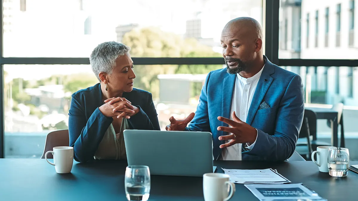 Two people sitting, talking in front of a laptop