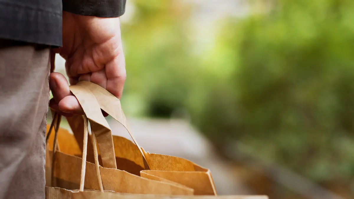 A hand holds a paper bag with thick handles