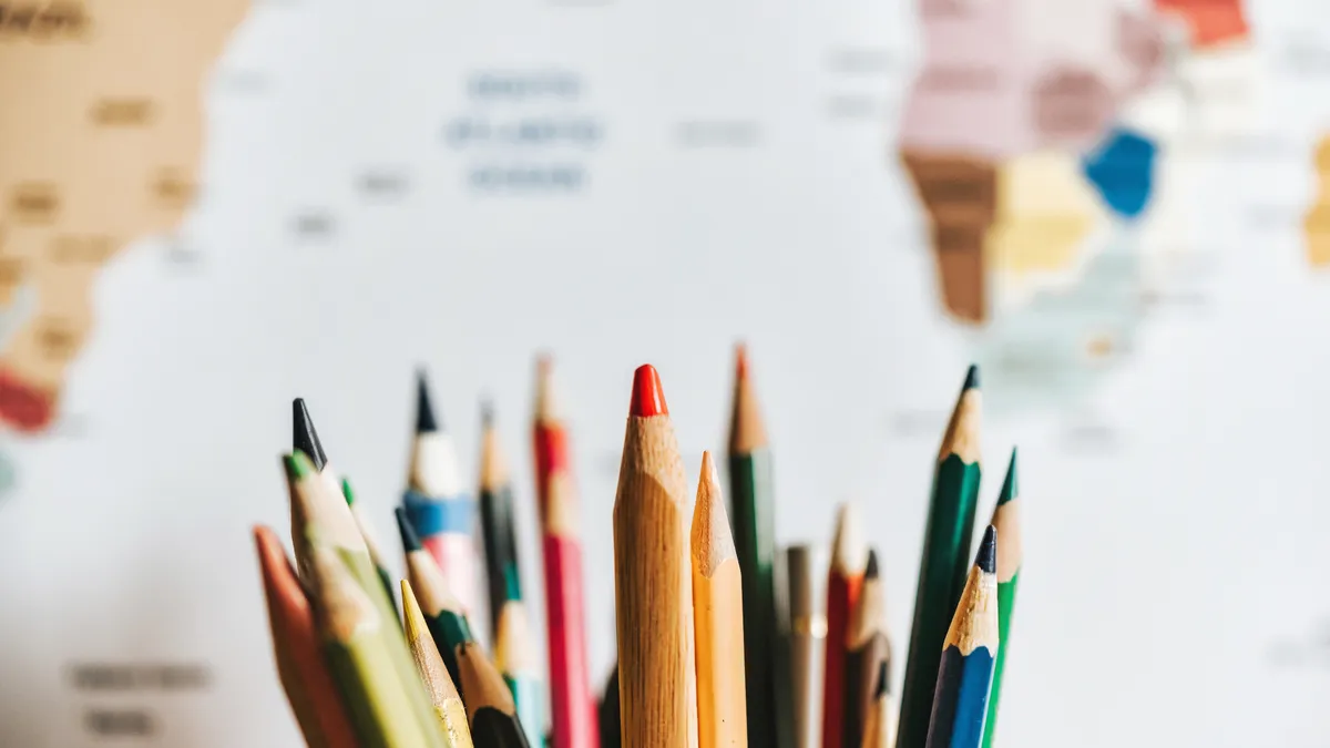 close up of various wooden colored pencils in beaker on desk in front of world map