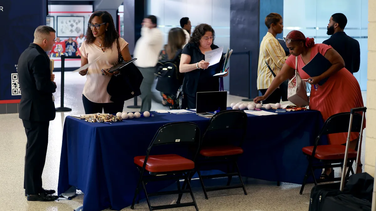 Individuals chat and trade documentation at a job fair table.