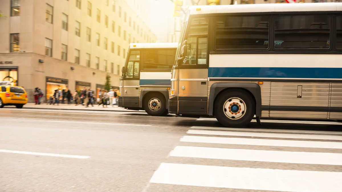 Two city buses are seen from a low angle at a crosswalk in a busy street.