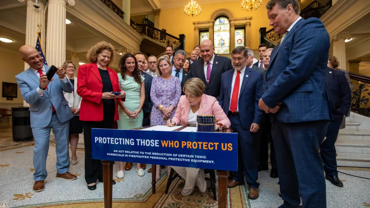 A person in the center sitting at a desk signing a document, with a group of people behind her.